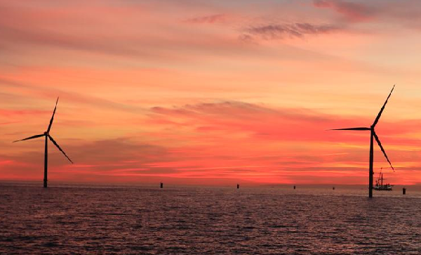 A sunset view over the sea with two wind turbines in the background